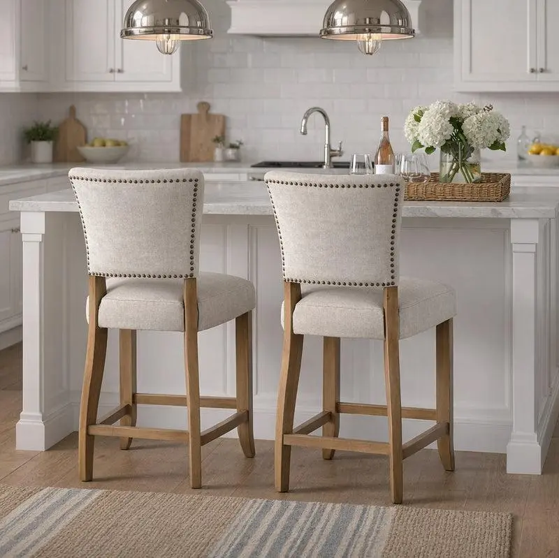 Two upholstered linen counter stools with light wood frames and footrests at a white kitchen island.